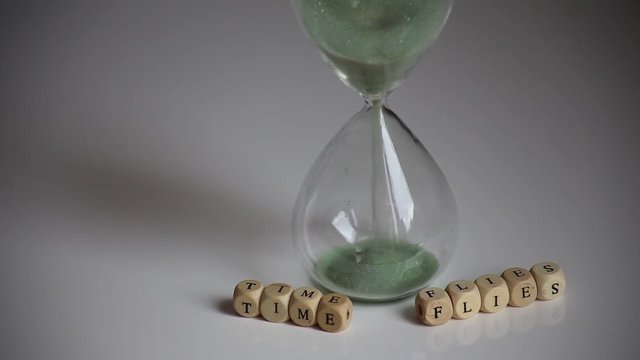 "Time Flies" mit Holzbuchstaben vor ablaufender Sanduhr