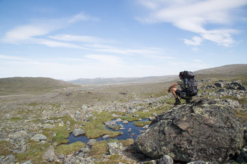 Fototapeta na wymiar Hiker squats on a rock, view from southwest towards the nature reserve Ráisduottarháldi, near Guolasjávri, Haltitunturi, summer 