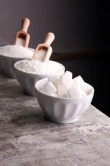 Bowl with white sand and lump sugar on grey background