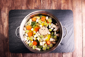 Broth with carrots, onions various fresh vegetables in a pot - colorful fresh clear spring soup. Rural kitchen scenery vegetarian bouillon or stock