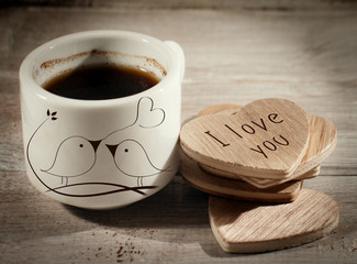 Close up cup of coffee with pair of lover birds design and writing I love you on wooden heart