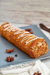 Swiss roll with sweet white cream on gray plate decorated with white cloth, star anise and  ripe carob fruit pods. Horizontal image. Side view