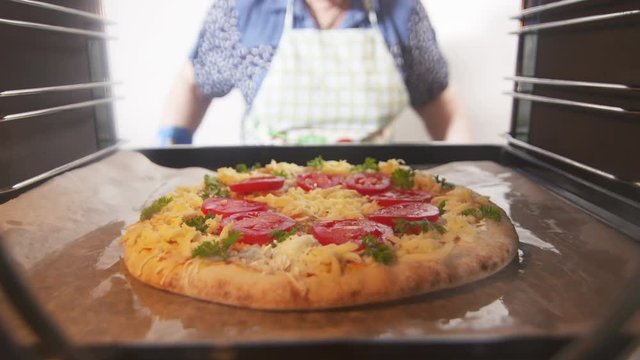 Cooking italian pizza in hot convection oven. Woman chef placing pizza on baking sheet inside hot oven. Frozen pizza topped with tomatoes mozzarella and edam cheese. Interior of electric cooker