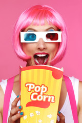 femme avec perruque rose et lunettes 3D au cinéma mangeant du pop-corn