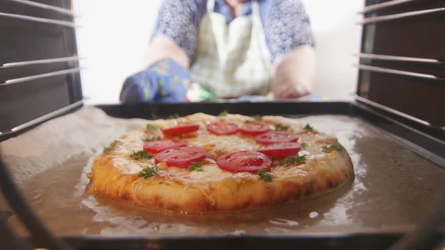 Baked italian pizza in convection oven. Woman opens cooker door and takes cooked ristorante pizza out of the hot oven. Toasty pizza topped with tomatoes mozzarella and edam cheese.