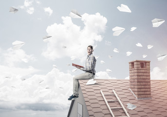 Man on brick roof reading book and paper planes flying in air