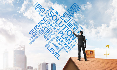 Fototapeta premium Young businessman standing on house roof and writing leadership skill concept. Mixed media