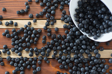Bowl full of aronia spilled on wooden table