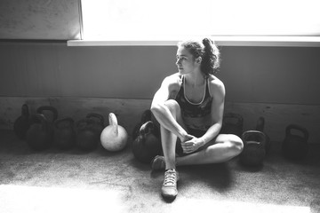 Obraz premium Young woman sitting by weights on gyms floor