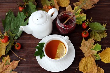 Tea with lemon and jam on table with autumn leaves