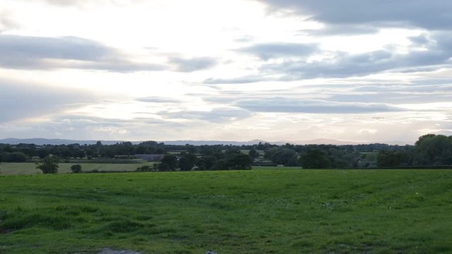 Rural landscape with green grass meadow, Tarvin, Cheshire, England, UK. Overcast sky with mountains and hills in background.