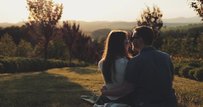 Young Couple Dream about Future in Fairytale Garden at Sunset. SLOW MOTION 4K. Romantic Man and Woman kiss and share lifetime plans. New Family. Love and affection. Cinematic shot, lens flare.