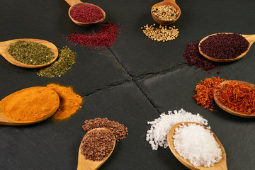 Colorful indian spices in wooden spoons on dark stone background