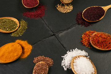 Colorful indian spices in wooden spoons on black stone background