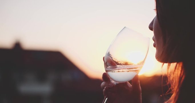 Woman Drinking Cooled White Wine from a glass at the Balcony during Sunset. Slow Motion 120 fps, 4K DCi. Beautiful female enjoying cozy evening on terrace. Summertime relax at sunny patio. Lens Flare