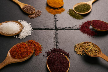 Colorful indian spices in wooden spoons on black stone background