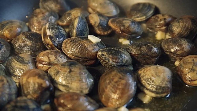 Close up of delicious clams in their shells cooked for a colourful seafood stir fry meal. Stewing mussels in a black frying pan on a hot plate.