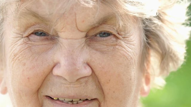 Portrait of smiling mature elderly woman with gray hair outdoors in the park in summer. Close-up