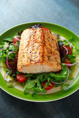 Baked salmon steak with tomato, onion, mix of green leaves salad in a plate. healthy food