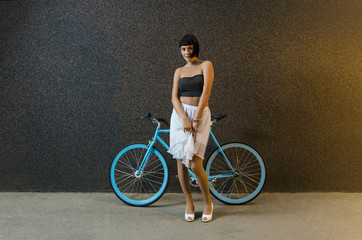 Fototapeta na wymiar Pretty young trendy woman posing with bicycle next to modern black stone wall 