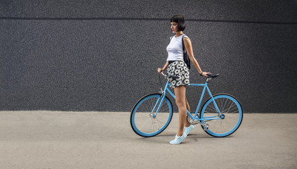 Urban hipster girl with all blue bicycle next to modern wall, copy space 