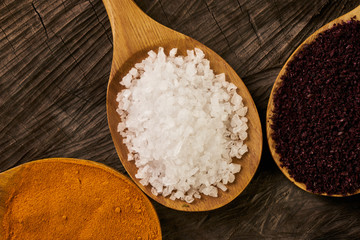 Colorful spices in wooden spoons on dark wooden background