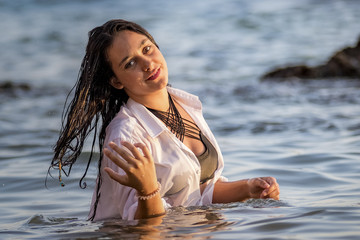 Chica joven con camisa blanca bañándose en el mar al atardecer.