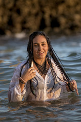 Chica joven con camisa blanca bañándose en el mar al atardecer.