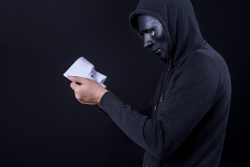 Mystery man wearing black mask holding and looking at white mask. Anonymous social masking or halloween concept.