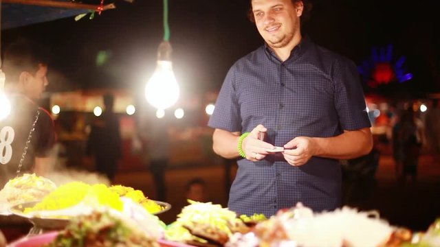 Cheerful man buys street food on asian buffet at night market. HD, 1920x1080