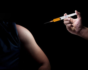 The Doctor's used syringe being to the act of injected medicine into the patient's shoulder. Liquid drug or narcotic. On a black background with copy space. Medical concept.