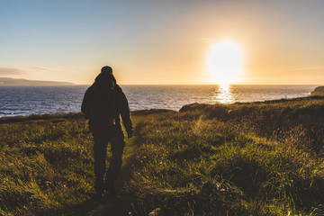 Man with backpack walking toward the sea at sunset