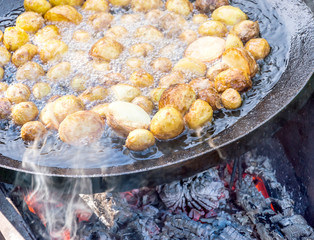 Young potatoes frying in oil in a large frying pan on fire. Cooking outdoors.