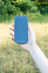 A woman's hand holds a smartphone in the park.