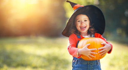 child girl with pumpkin outdoors in halloween.