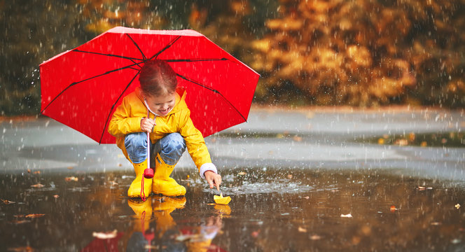 happy child girl with umbrella and paper boat in   puddle in   autumn on nature