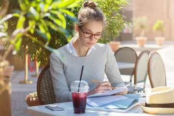 Closeup picture of young beautiful business woman working with papers while sitting at outdoor café table, looking very serious and attentive concentrated not to make any mistakes while checking