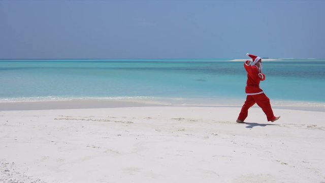 Man in Santa Claus Hat running and jumping along the beach. Christmas vacation on Maldivian islands