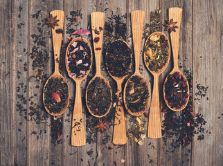 arious kinds of tea in wooden spoons on weathered wood background top view.