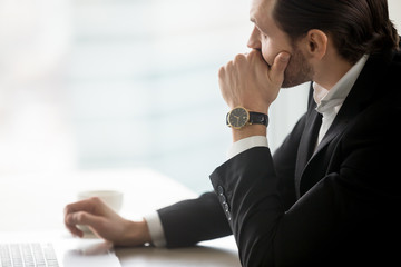 Serious concerned young businessman looks towards the window in deep thought sitting at workplace...