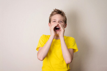 Happy teen boy in yellow t-shirt shout and scream using his hands as tube, studio shoot isolated on white.