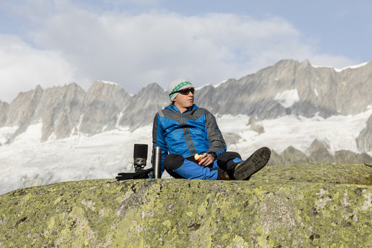 Alpinist makes a break in the mountains, eats an apple and enjoys freedom in nature