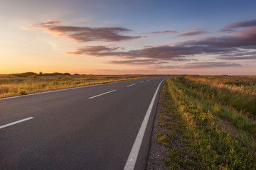 Fototapeta na wymiar Curved asphalt road in plain at idyllic sunset