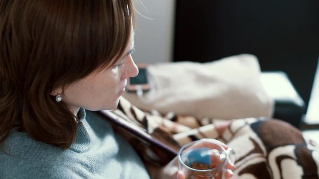 A cold woman drinks a decoction of herbs. The sick girl was wrapped in a blanket.