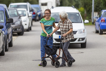 Seniorin am Rollator überquert mit ihrer Enkelin die Straße - obrazy, fototapety, plakaty