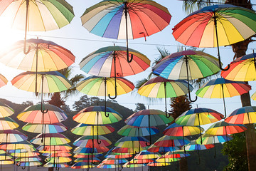 Fototapeta na wymiar Colorful umbrellas background. Multi-colored umbrellas in the sky floating above the street against palms trees.