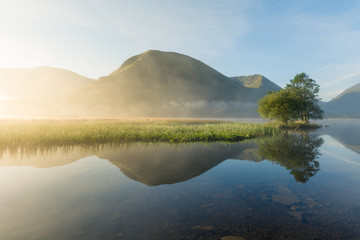 Clear reflections of mountains in lake on a misty summer morning at Brotherswater in the Lake District.
