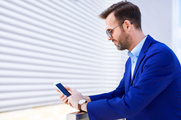 Side view of confident middle-aged businessman using phone in outside urban setting