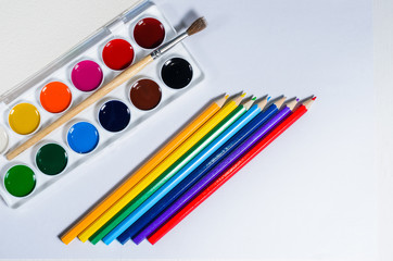 Bright colored watercolor paints and pencils, top view, white background.