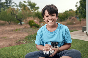 Boy with dark hair in summer outdoors. He is playing with a cat.
